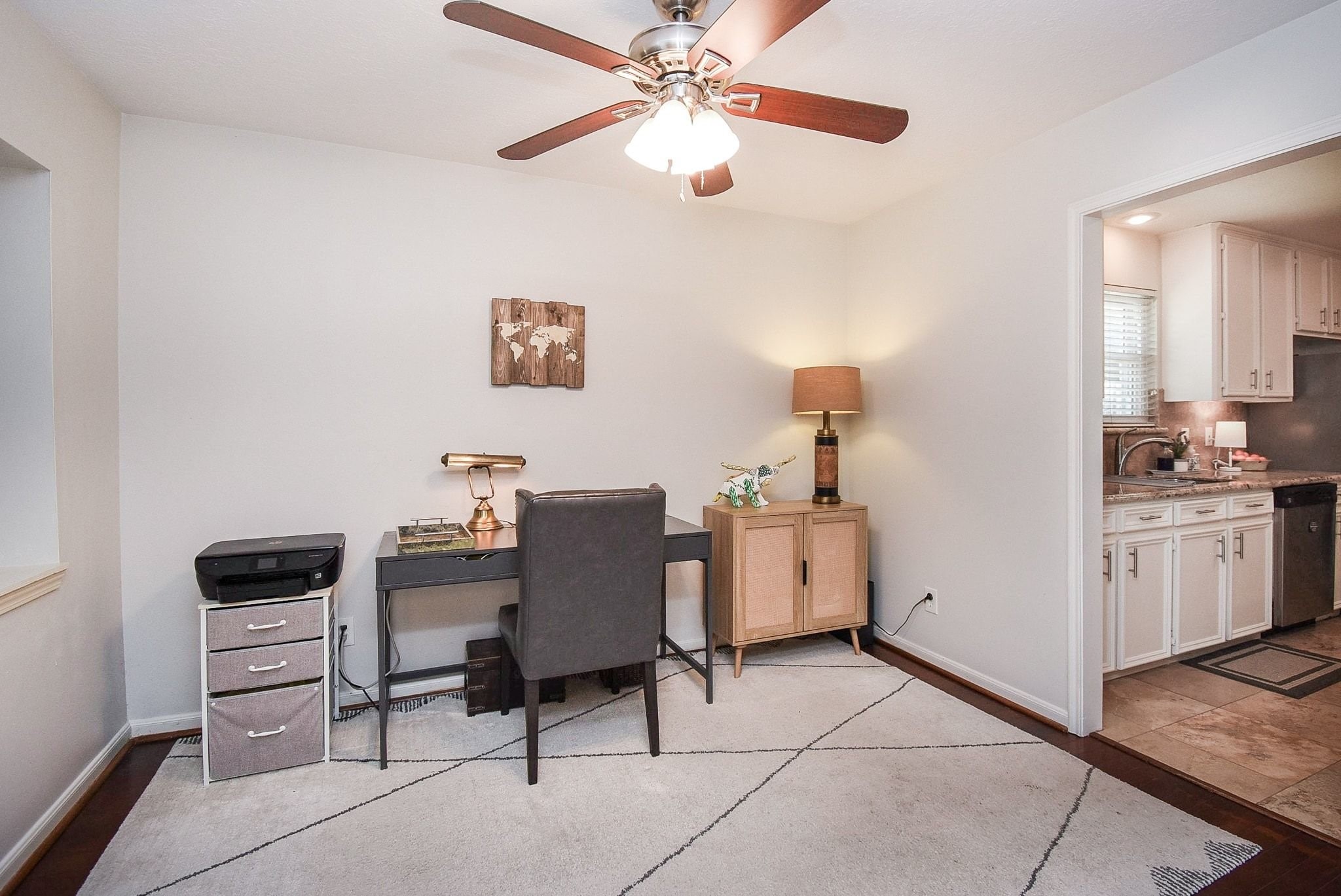 2930 Kevin Lane Houston, TX 77080 - Photo 21 of 50 This photo showcases a cozy home office/formal with a ceiling fan and ample lighting. The room has a view into a kitchen area with white cabinetry.