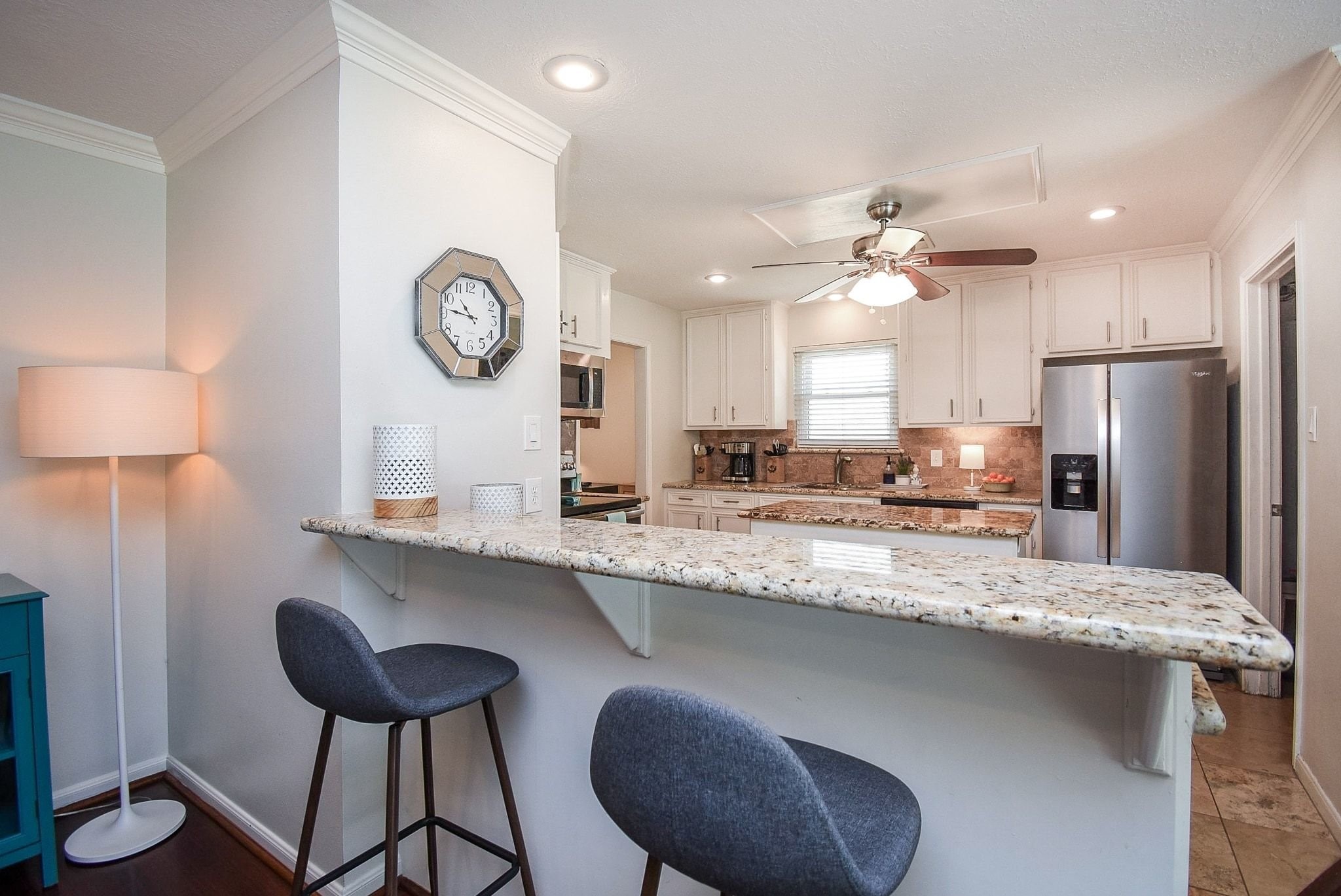 2930 Kevin Lane Houston, TX 77080 - Photo 29 of 50 This photo showcases a modern kitchen with a granite countertop bar, and white cabinetry. The space features stainless steel appliances, a ceiling fan, and ample lighting, creating a welcoming and functional area.