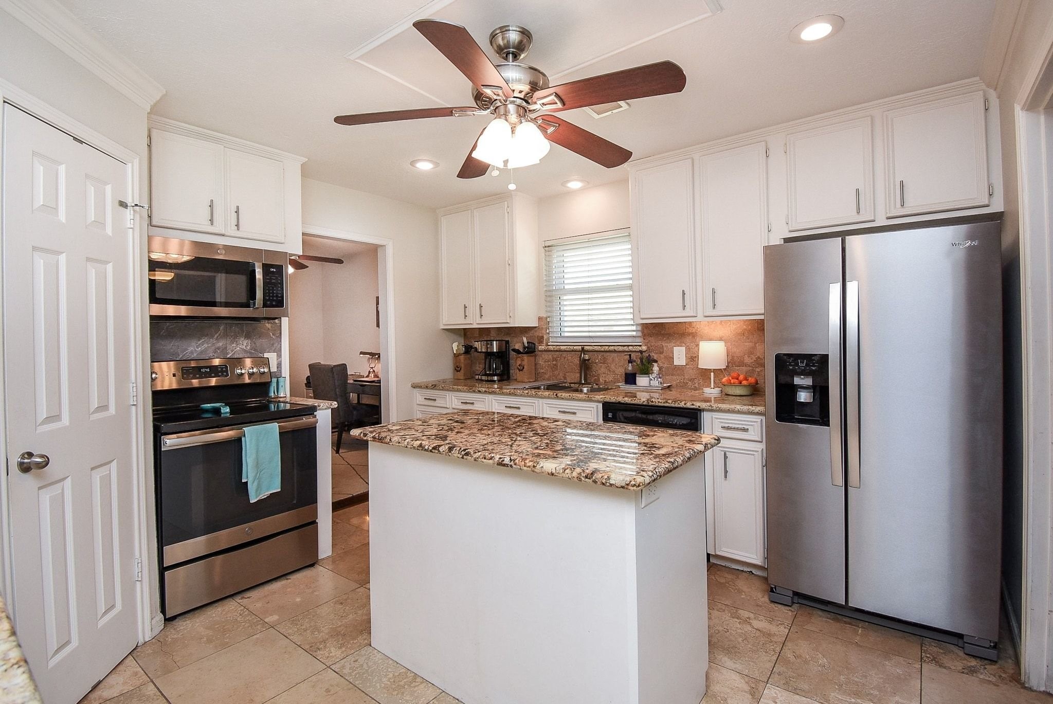 2930 Kevin Lane Houston, TX 77080 - Photo 30 of 50 This kitchen features modern stainless steel appliances, white cabinetry, and granite countertops. It includes a central island, a ceiling fan with lighting, and tiled flooring, offering a bright and functional space.