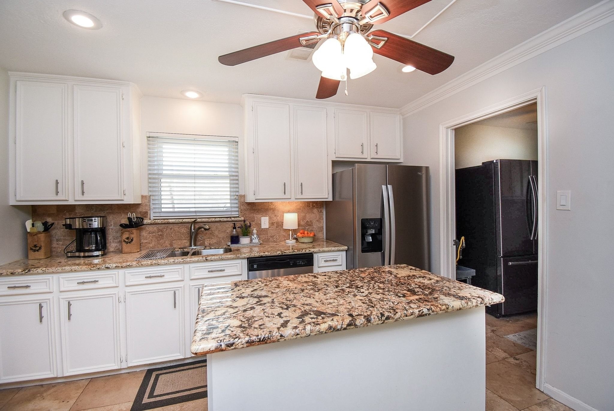 2930 Kevin Lane Houston, TX 77080 - Photo 32 of 50 This kitchen features granite countertops, white cabinetry, stainless steel appliances, and a central island. It has a ceiling fan with lights and a window for natural light, creating a bright and welcoming atmosphere.