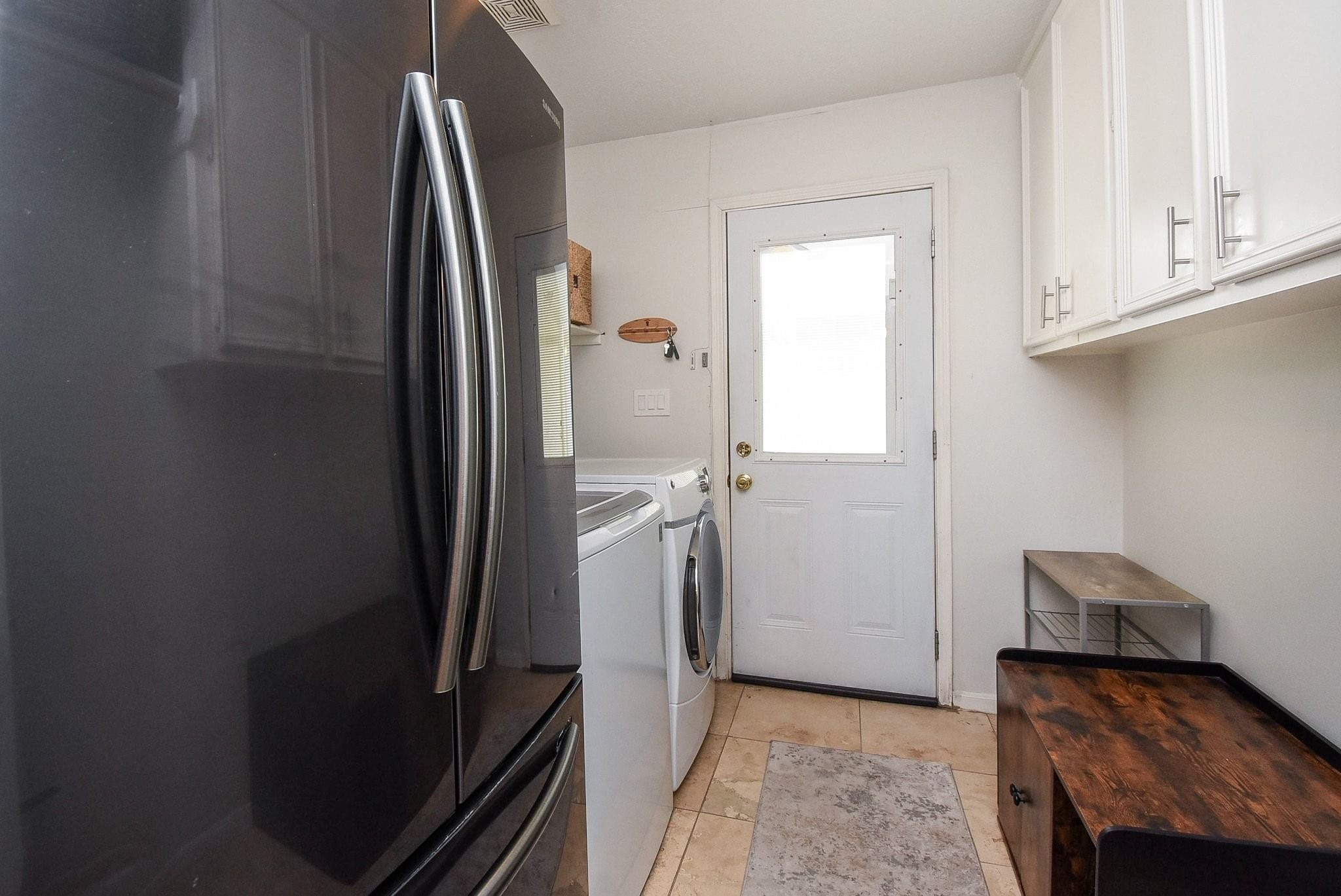 2930 Kevin Lane Houston, TX 77080 - Photo 33 of 50 This photo showcases a compact laundry room with a washer and dryer, white cabinets for storage, and a space for a refrigerator. The room features tile flooring and a door leading outside, offering convenience and functionality.