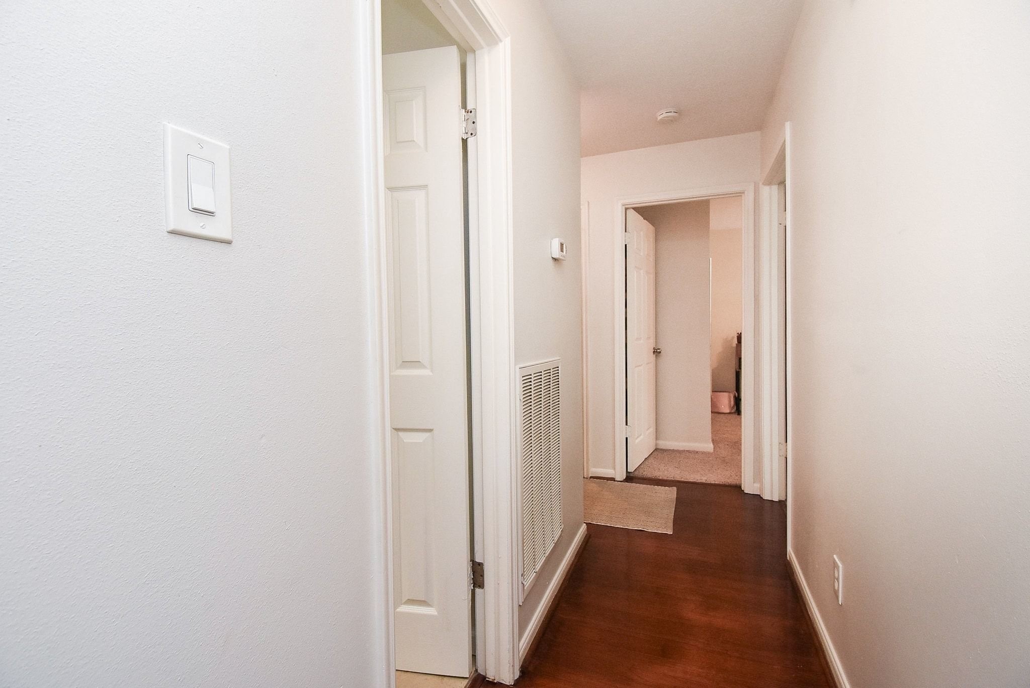 2930 Kevin Lane Houston, TX 77080 - Photo 34 of 50 This photo shows a clean, well-lit hallway with hardwood flooring leading to multiple rooms. The walls are painted in a neutral color, and there are white doors providing access to adjacent rooms.
