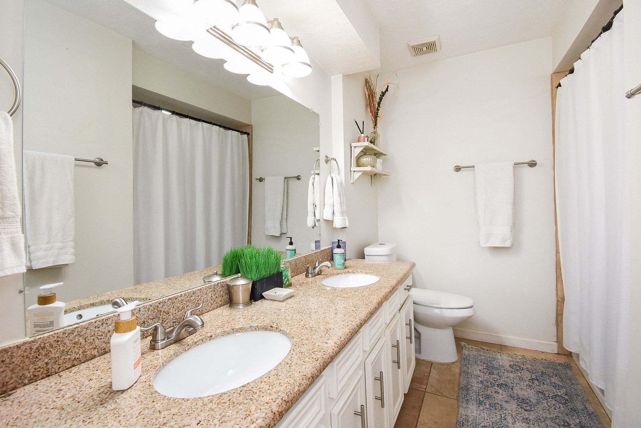 2930 Kevin Lane Houston, TX 77080 - Photo 35 of 50 This bathroom features a double sink vanity with granite countertops, ample cabinet storage, and modern lighting. It includes a shower-tub combo with a curtain and has a clean, neutral design.