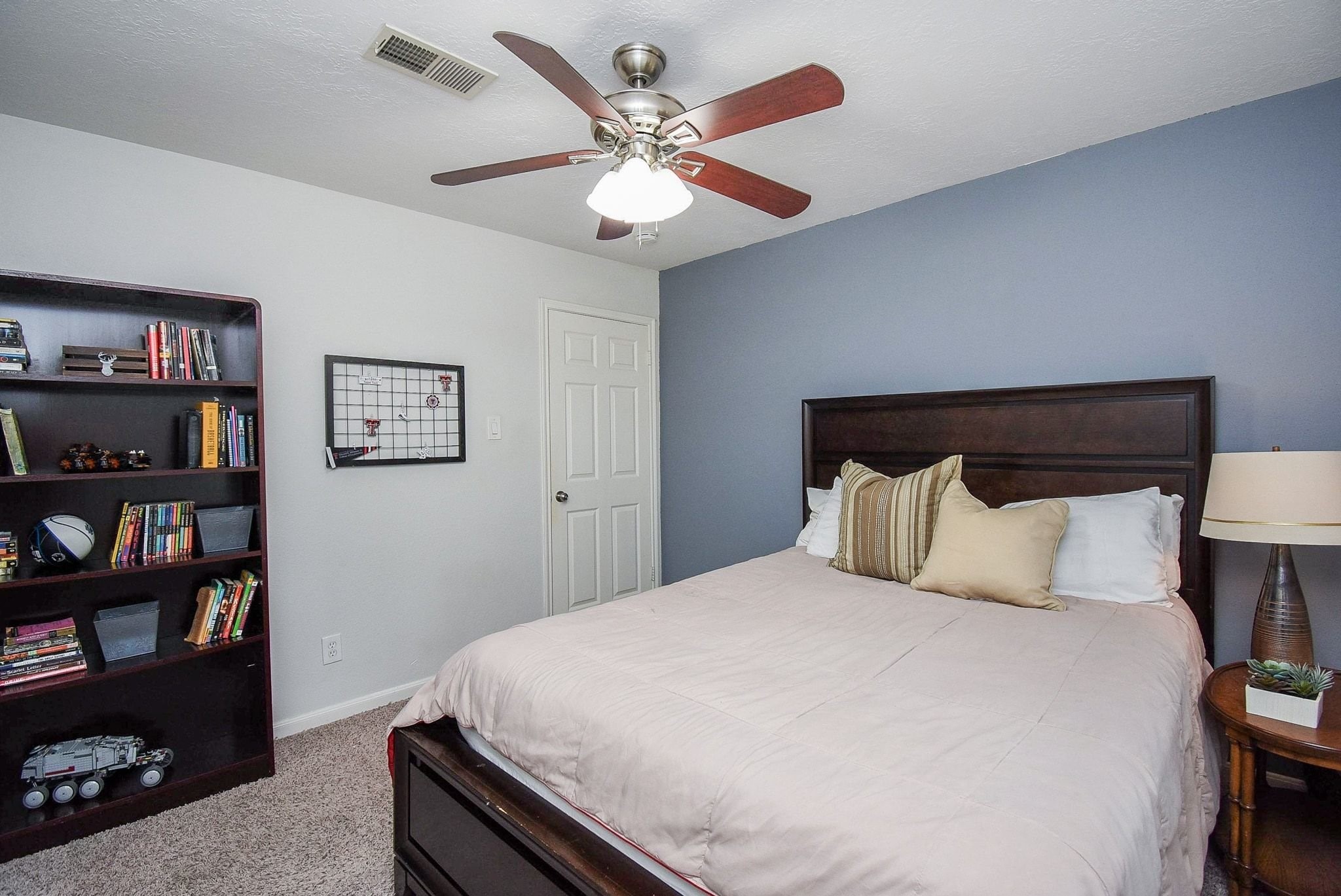2930 Kevin Lane Houston, TX 77080 - Photo 38 of 50 This cozy bedroom features a modern ceiling fan, a soft blue accent wall, and a comfortable bed with plush pillows. It has a warm and inviting atmosphere.