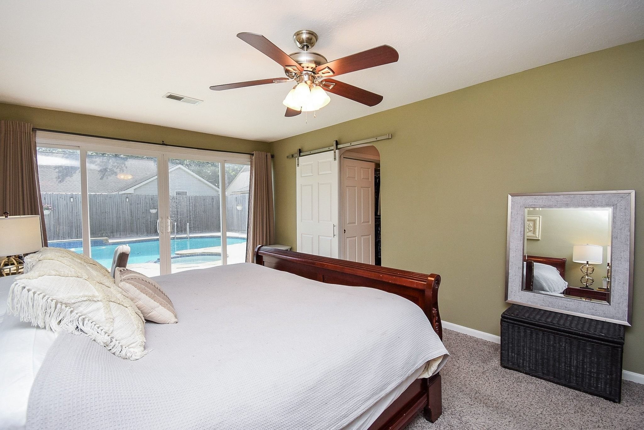2930 Kevin Lane Houston, TX 77080 - Photo 47 of 50 This bedroom features a cozy carpeted floor, large sliding glass doors leading to a pool view, a ceiling fan, and a barn-style door to the ensuite. It has neutral tones and a spacious layout.