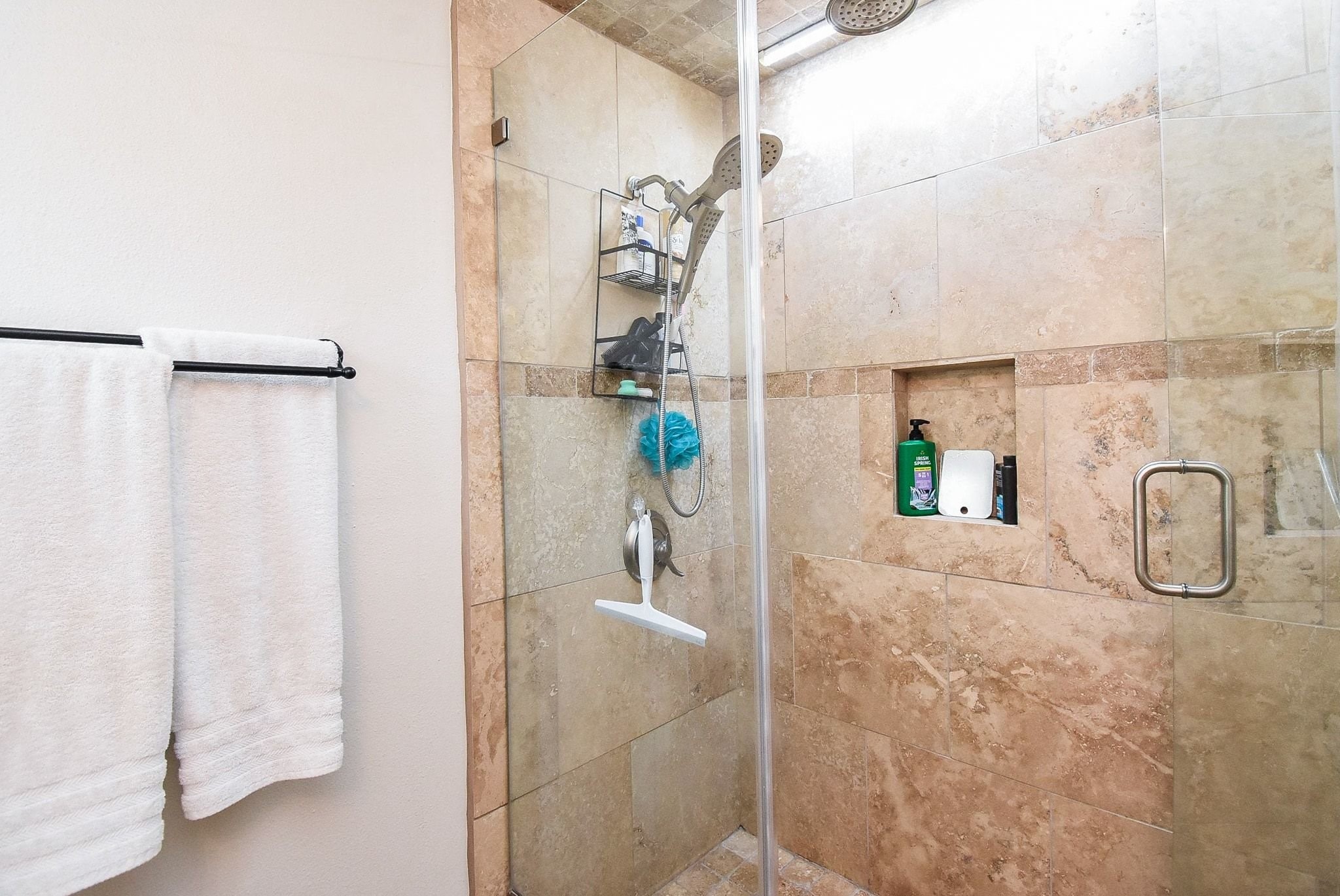 2930 Kevin Lane Houston, TX 77080 - Photo 49 of 50 This bathroom features a spacious, glass-enclosed shower with elegant beige tile, dual showerheads, and built-in shelving. It includes a convenient towel rack with fresh white towels, offering both functionality and style.