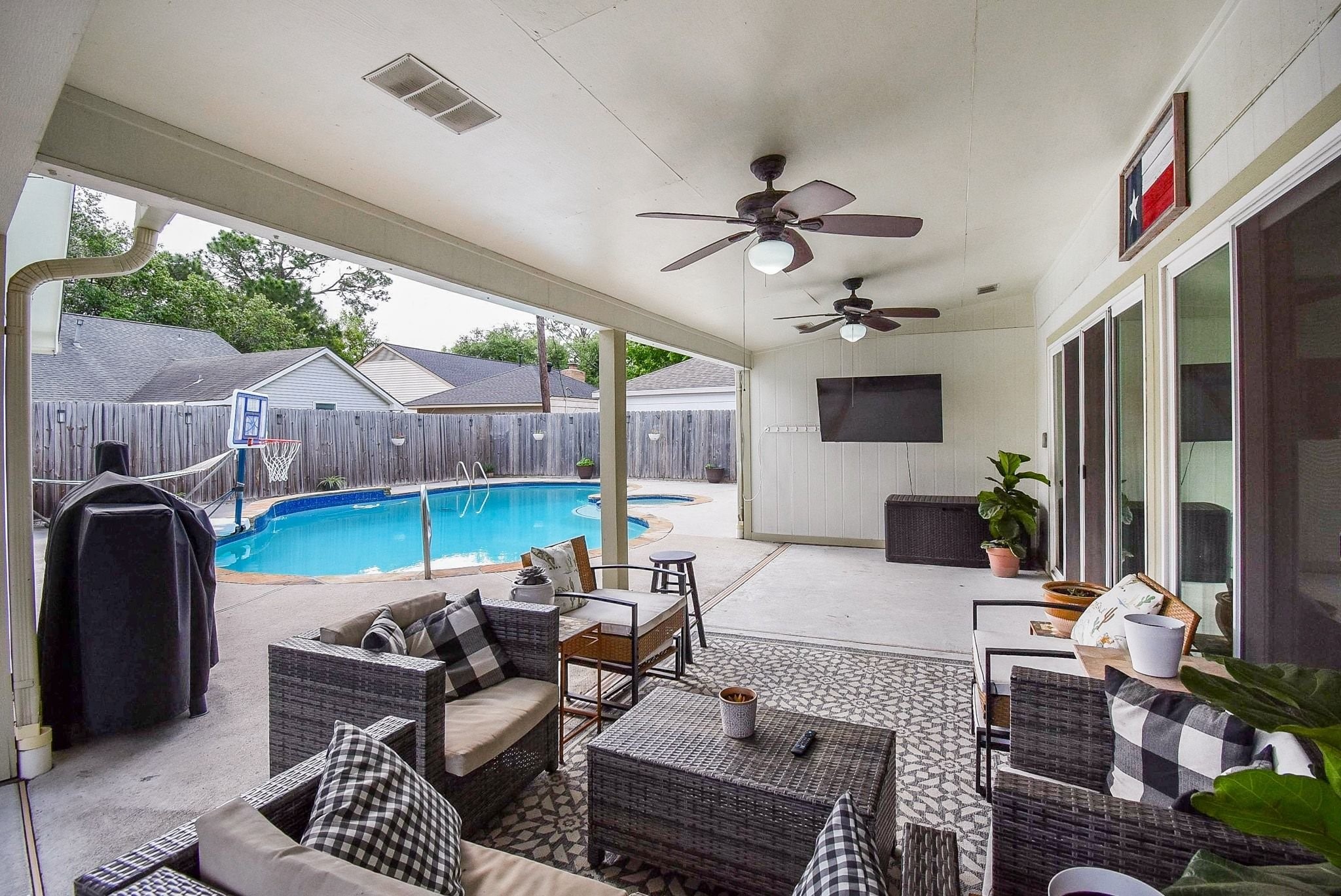2930 Kevin Lane Houston, TX 77080 - Photo 10 of 50 This photo showcases a covered patio with stylish outdoor seating, ceiling fans, and a mounted TV. It overlooks a fenced backyard featuring a pool, creating a perfect space for relaxation and entertainment.