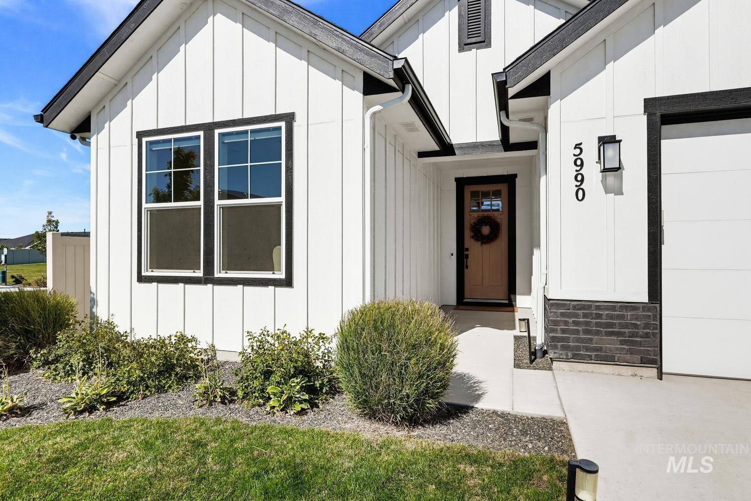 5990 West Ladle Rpds Street Meridian, ID 83646 - Photo 3 of 42 White board and batten siding, dark trim accents, brick detailing, natural wood-finish front door, and a clean concrete pathway