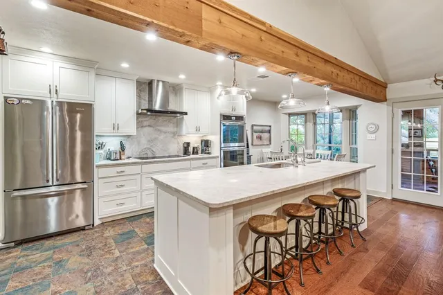 a kitchen with stainless steel appliances granite countertop a refrigerator a sink dishwasher a stove and white cabinets with wooden floor