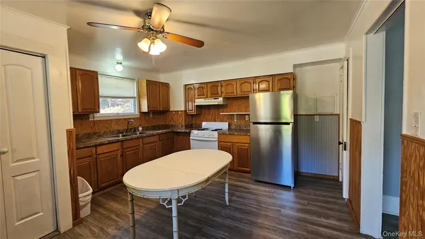 a kitchen with stainless steel appliances a refrigerator a sink a stove a dining table and chairs with wooden floor