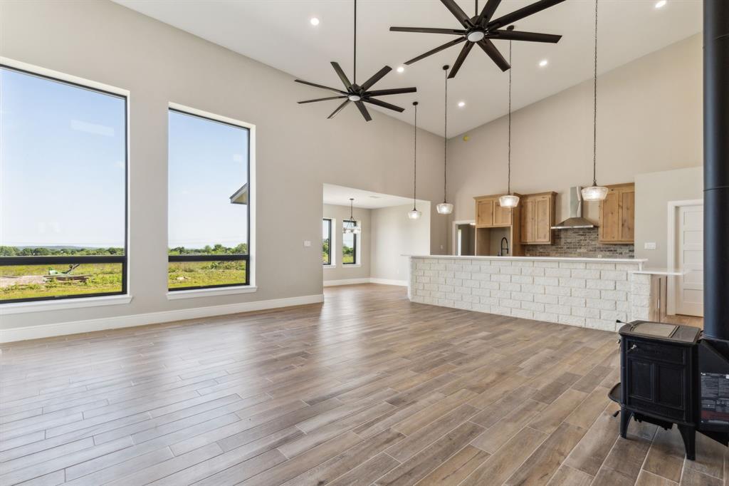 700 Brown Road Palo Pinto, TX 76484 - Photo 12 of 40 Living room featuring a towering ceiling, big windows with natural light, wood look tile floors, a wood stove, baseboards, and ceiling fan