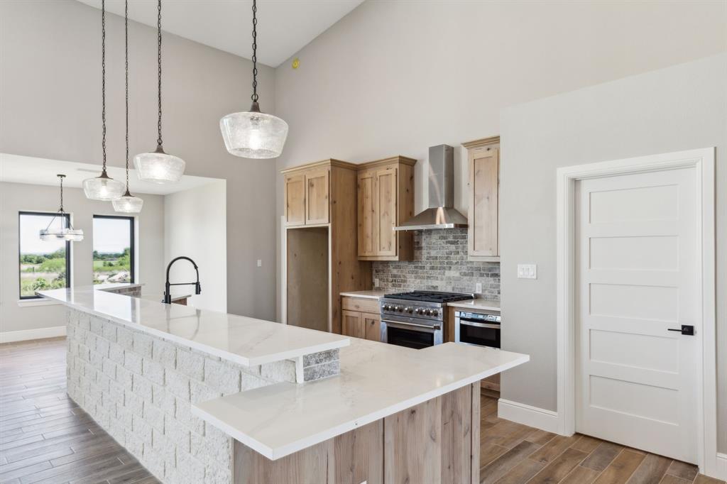 700 Brown Road Palo Pinto, TX 76484 - Photo 5 of 40 Kitchen featuring wood look tile floors, high end stainless steel range, range hood, baseboards, and high vaulted ceiling, island and door to pantry
