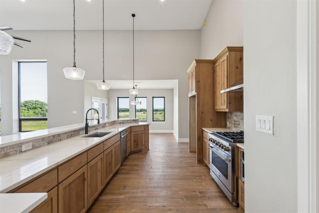 700 Brown Road Palo Pinto, TX 76484 - Photo 6 of 40 Kitchen with wood look tile floors, stainless steel appliances, a sink, decorative backsplash, and hanging light fixtures