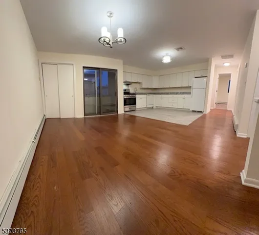 a view of empty room with wooden floor and kitchen