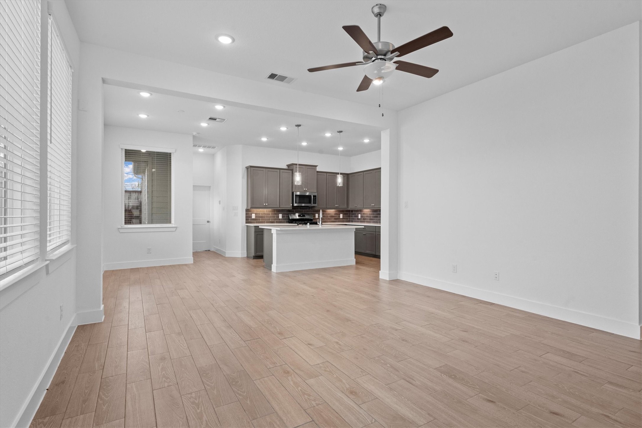 120 Red Cascade Trail Willis, TX 77318 - Photo 7 of 37 This photo showcases a modern living space with sleek wood look flooring, a ceiling fan, and ample natural light from large windows. A stylish staircase with black railing leads to the upper level, and a bold front door adds a contemporary touch.