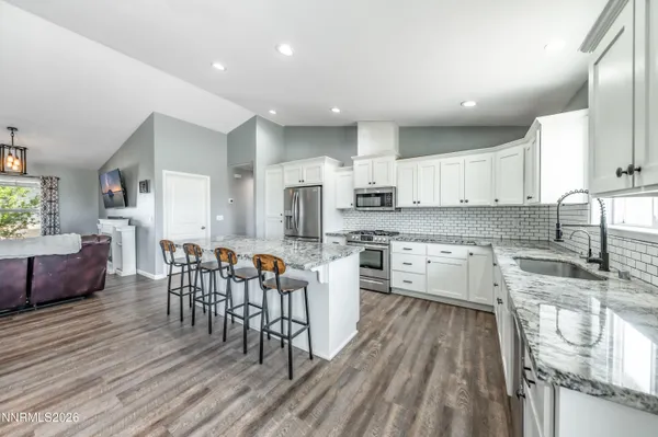 a kitchen with stainless steel appliances granite countertop a stove top oven a sink dishwasher a dining table and chairs with wooden floor