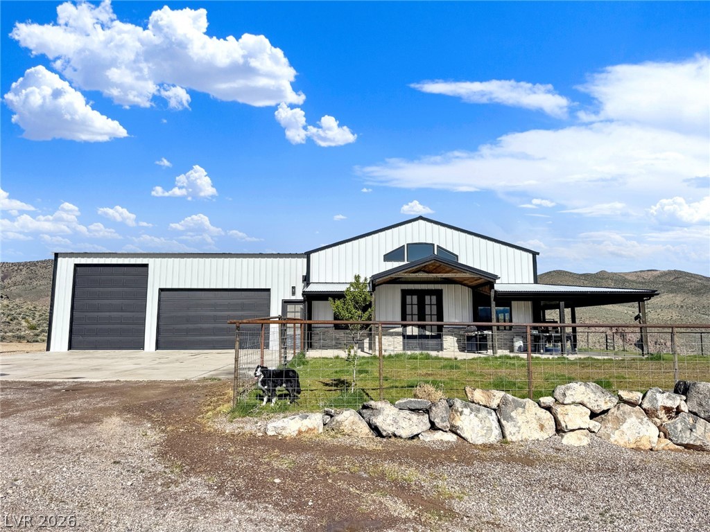 9393 North 93rd Highway Caliente, NV 89008 - Photo 6 of 41 A modern rural retreat boasts expansive garage doors and a wide covered porch, set against a backdrop of rolling hills.