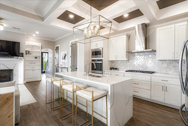 a kitchen with stainless steel appliances granite countertop a stove top oven a refrigerator a sink and white cabinets with wooden floor