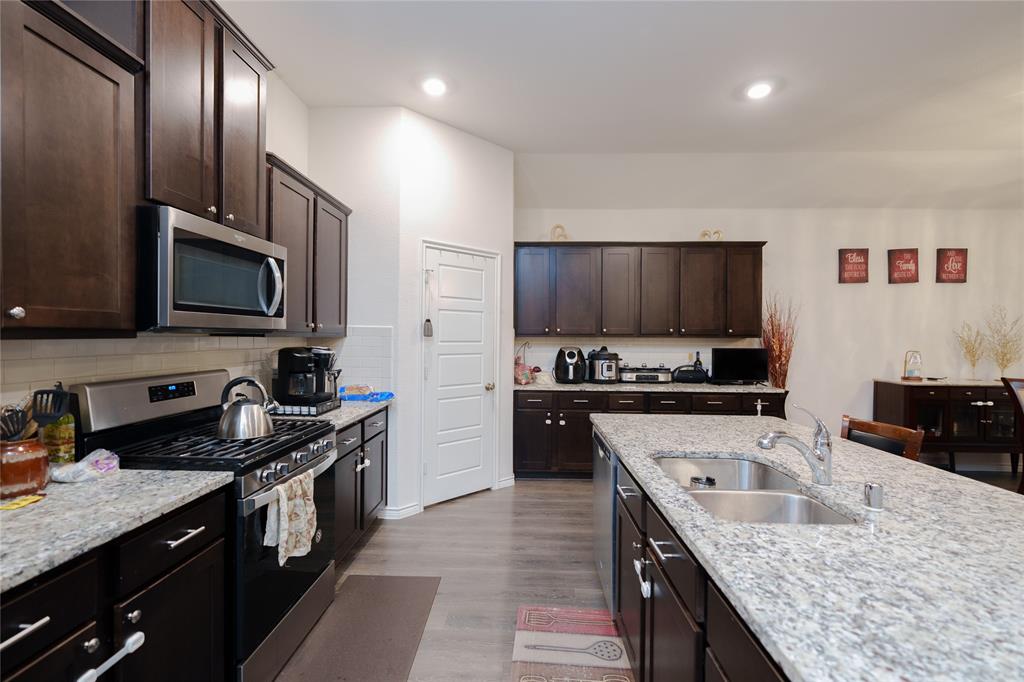 4009 Forest Bend Road Denton, TX 76208 - Photo 6 of 35 Kitchen featuring stainless steel appliances, dark wood finish cabinetry, light wood-style flooring, light stone counters, and recessed lighting