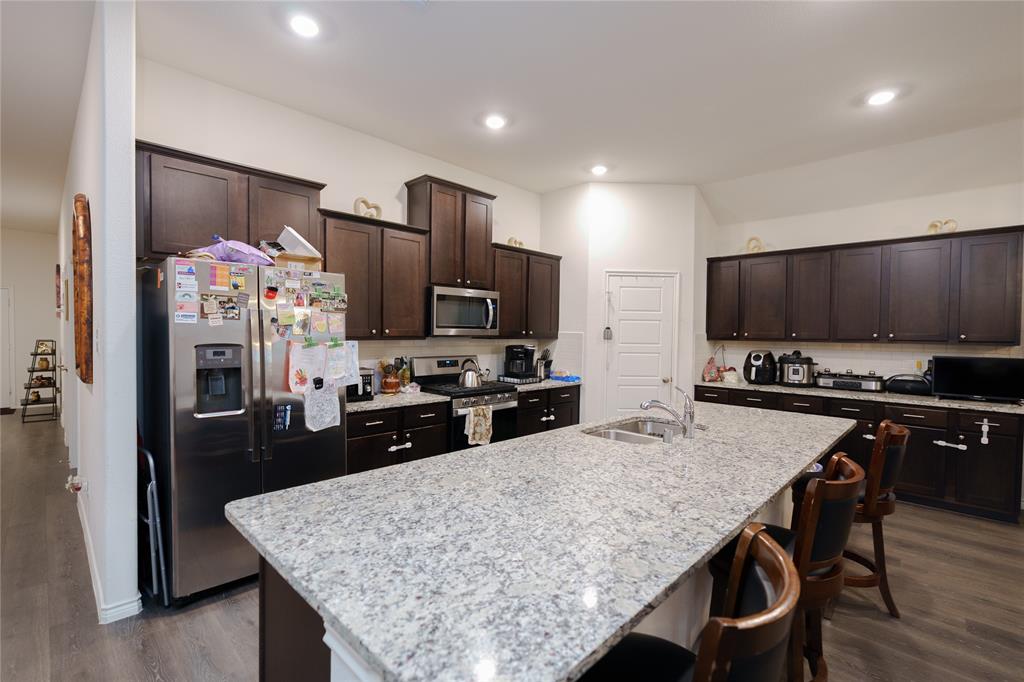 4009 Forest Bend Road Denton, TX 76208 - Photo 8 of 35 Kitchen with dark wood finish cabinetry, stainless steel appliances, light stone countertops, dark wood-style floors, and a kitchen breakfast bar
