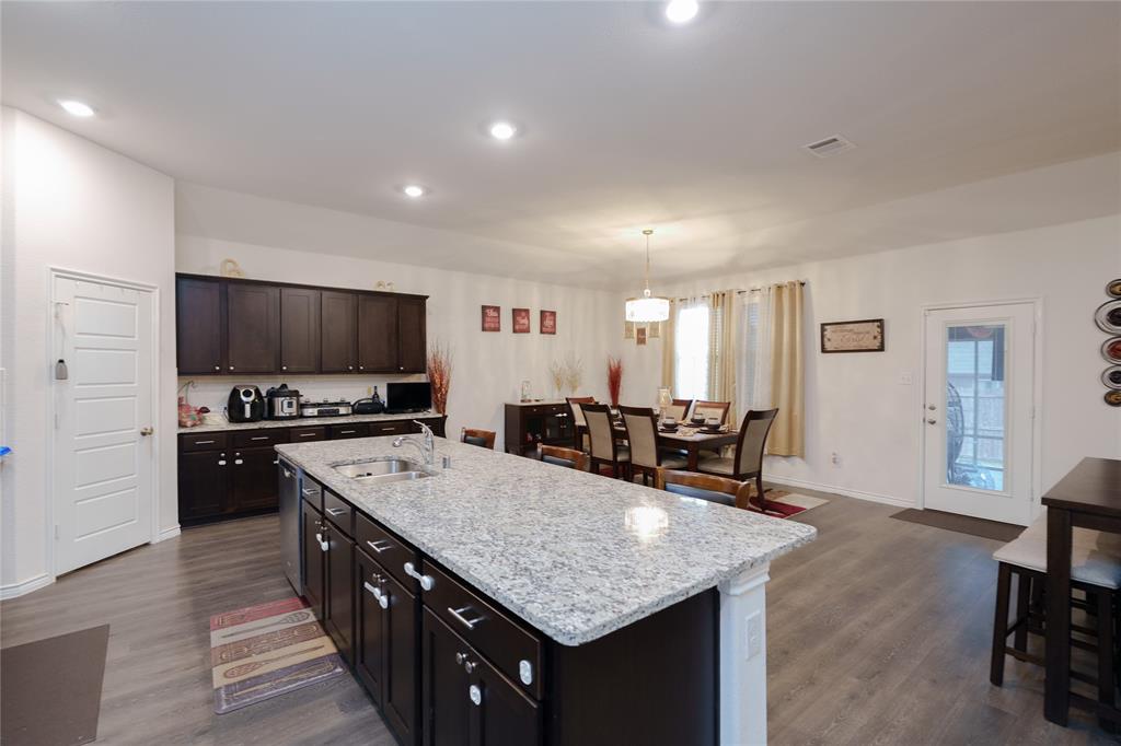 4009 Forest Bend Road Denton, TX 76208 - Photo 9 of 35 Kitchen with dark wood finish cabinetry, dark wood-type flooring, light stone counters, and hanging light fixtures