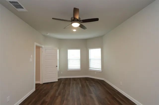 an empty room with wooden floor ceiling fan and windows