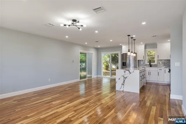 a view of an empty room and kitchen view with wooden floor