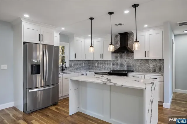 a kitchen with stainless steel appliances granite countertop a refrigerator a sink a stove and white cabinets with wooden floor