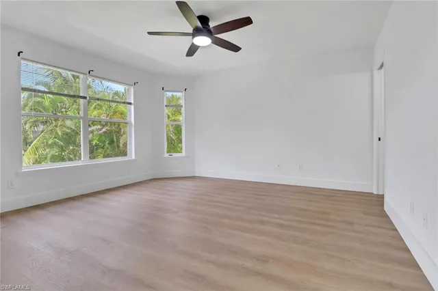 an empty room with wooden floor fan and windows