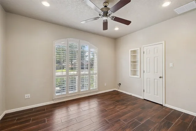 an empty room with wooden floor chandelier fan and windows