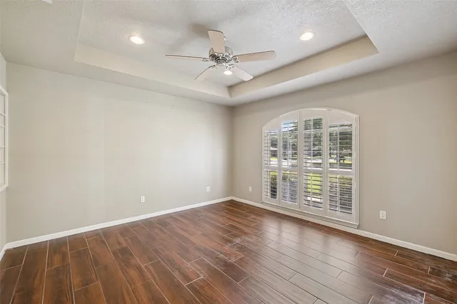 an empty room with wooden floor fan and windows
