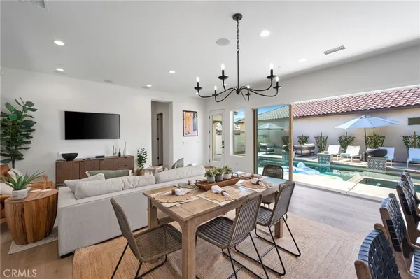 a view of a dining room and livingroom with furniture wooden floor a rug a flat screen tv and a chandelier