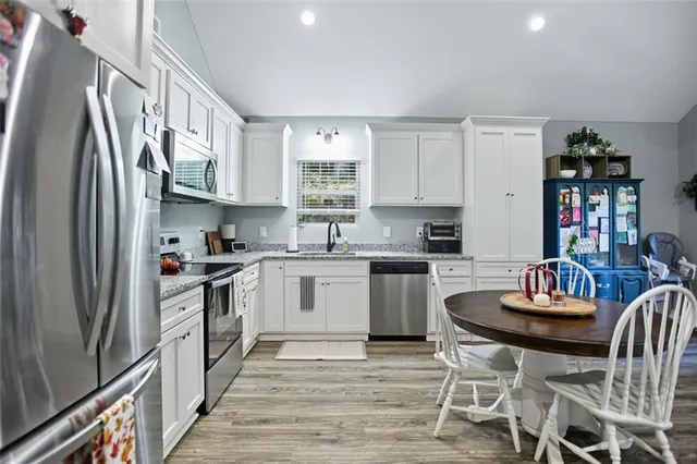 a kitchen with stainless steel appliances granite countertop a stove a sink dishwasher a refrigerator and white cabinets with wooden floor