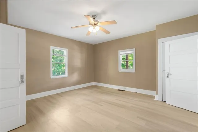 a view of an empty room with wooden floor and a ceiling fan