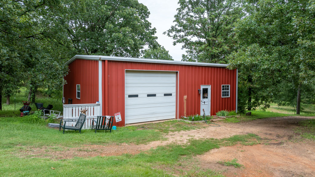 365 Calihan Road Booneville, AR 72927 - Photo 6 of 59 Red metal utility building featuring a white garage door, a side entry door, and a white-railed porch