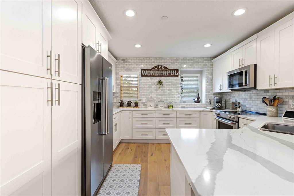 9040 White Sage Loop Lakewood Ranch, FL 34202 - Photo 38 of 59 a kitchen with stainless steel appliances kitchen island granite countertop a refrigerator oven a sink dishwasher and white cabinets with wooden floor