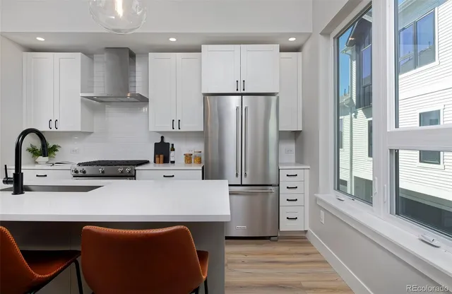 a kitchen with stainless steel appliances a refrigerator a sink a stove and white cabinets with wooden floor