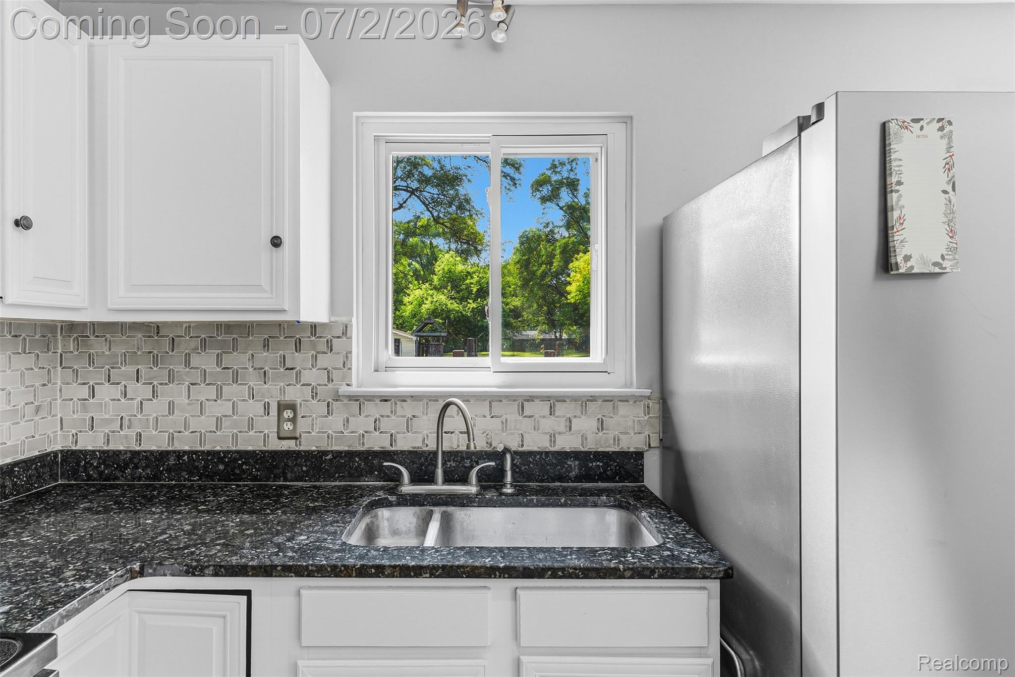 305 East Road Holly, MI 48442 - Photo 11 of 41 Kitchen sink area featuring a window, white cabinetry, a dual-basin stainless steel sink with a gooseneck faucet, dark speckled countertops, and a tiled backsplash