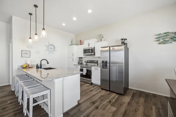 a kitchen with stainless steel appliances granite countertop a refrigerator a sink dishwasher a stove and a dining table with wooden floor