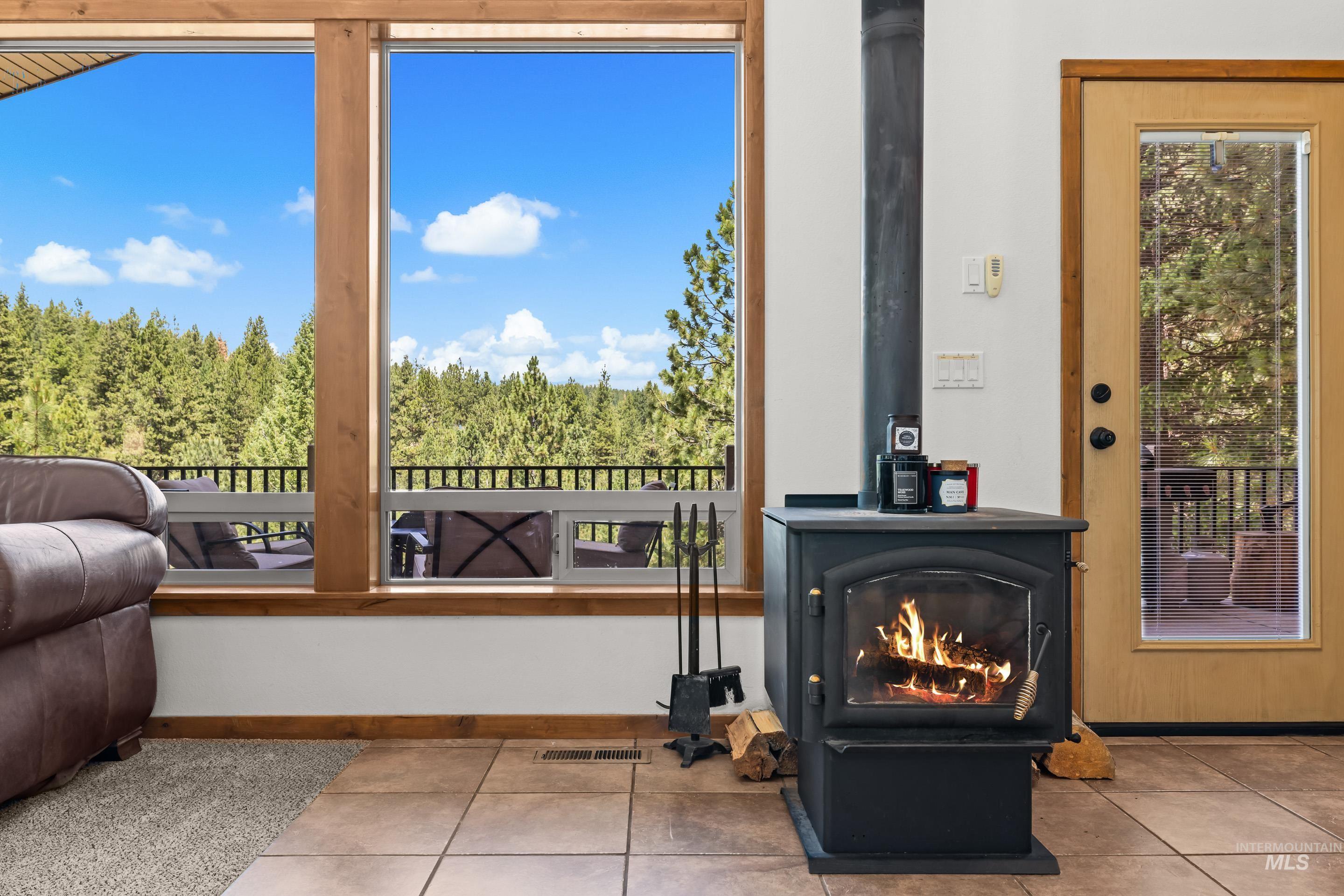 92 Cruickshank Road Horseshoe Bend, ID 83629 - Photo 12 of 50 Expansive windows with wood trim, a freestanding wood-burning stove with a hearth, and a glass-paneled exterior door