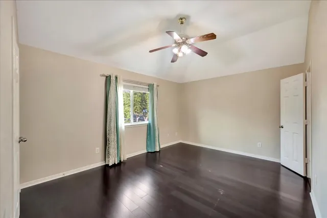 an empty room with wooden floor chandelier fan and windows