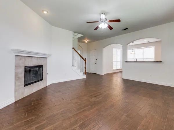 an empty room with wooden floor a ceiling fan a fireplace and windows