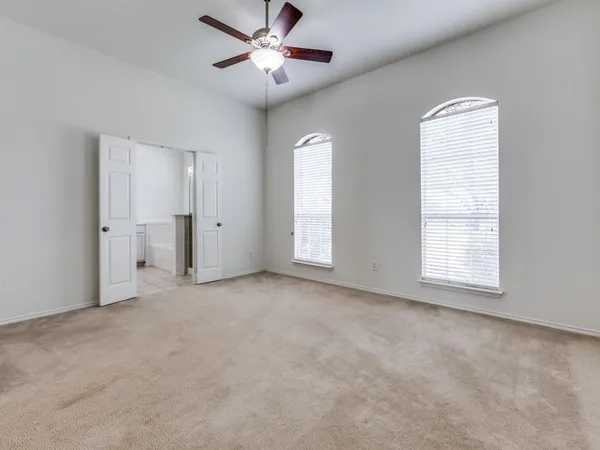 an empty room with chandelier fan and windows