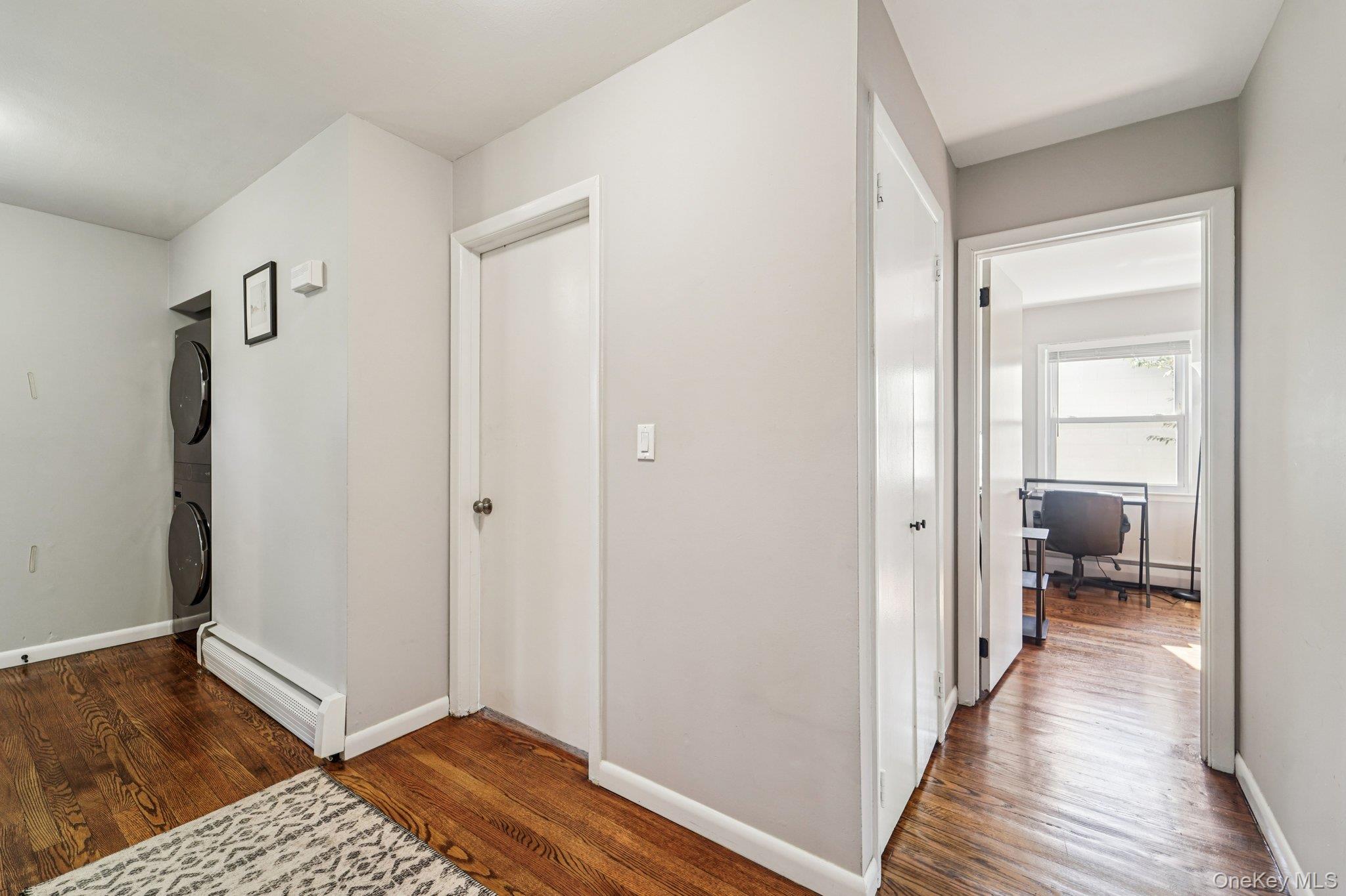 252 County Center Road White Plains, NY 10603 - Photo 14 of 44 Hallway with an office area, a baseboard radiator, dark wood-type flooring, and stacked washing machine and dryer
