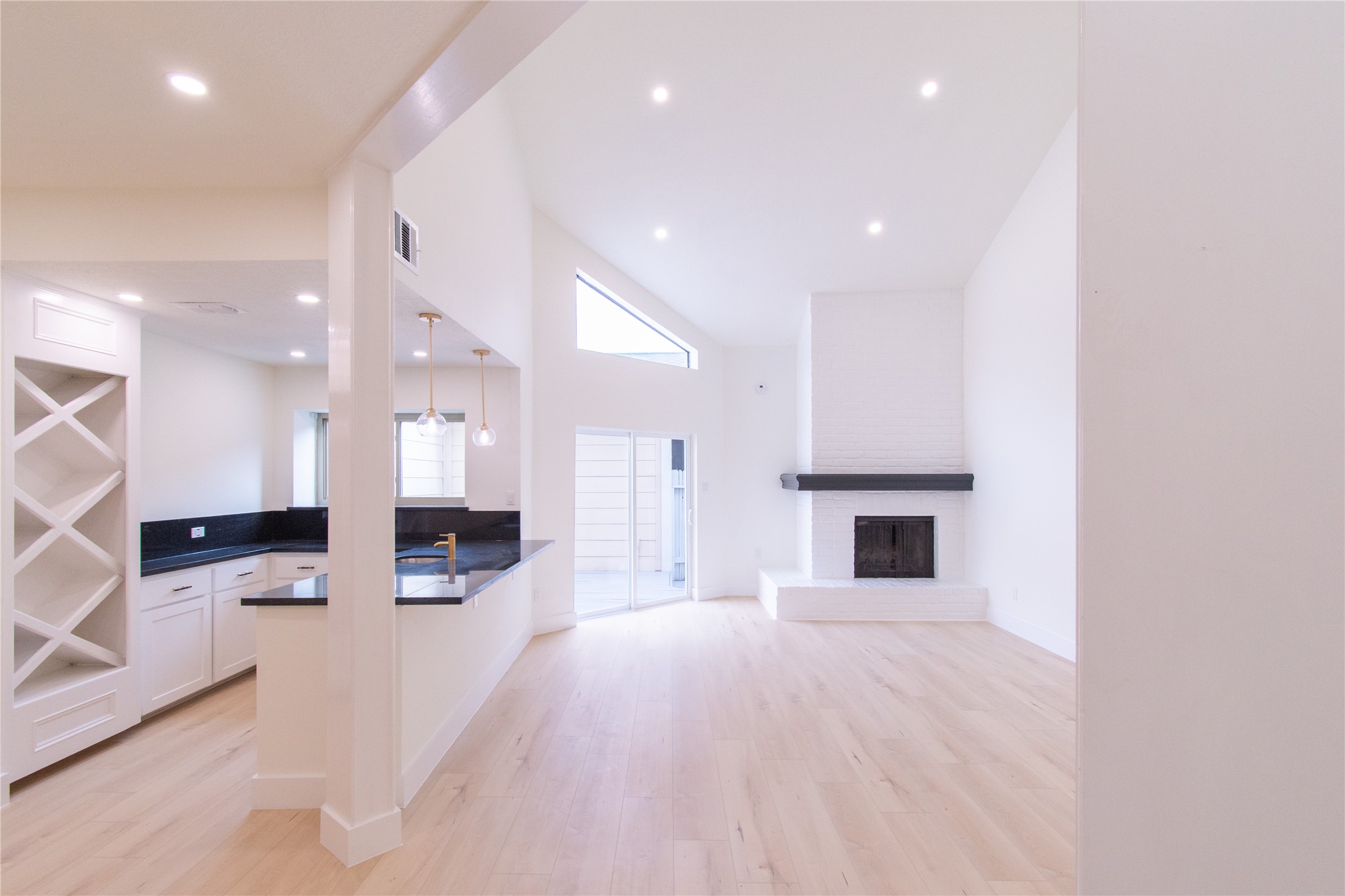 727 Bunker Hill Road, Unit 43 Houston, TX 77024 - Photo 1 of 34 Open-concept living space features a modern kitchen with a breakfast bar, a cozy brick fireplace, and high ceilings. Natural light pours in through large windows, complementing the light wood flooring.
