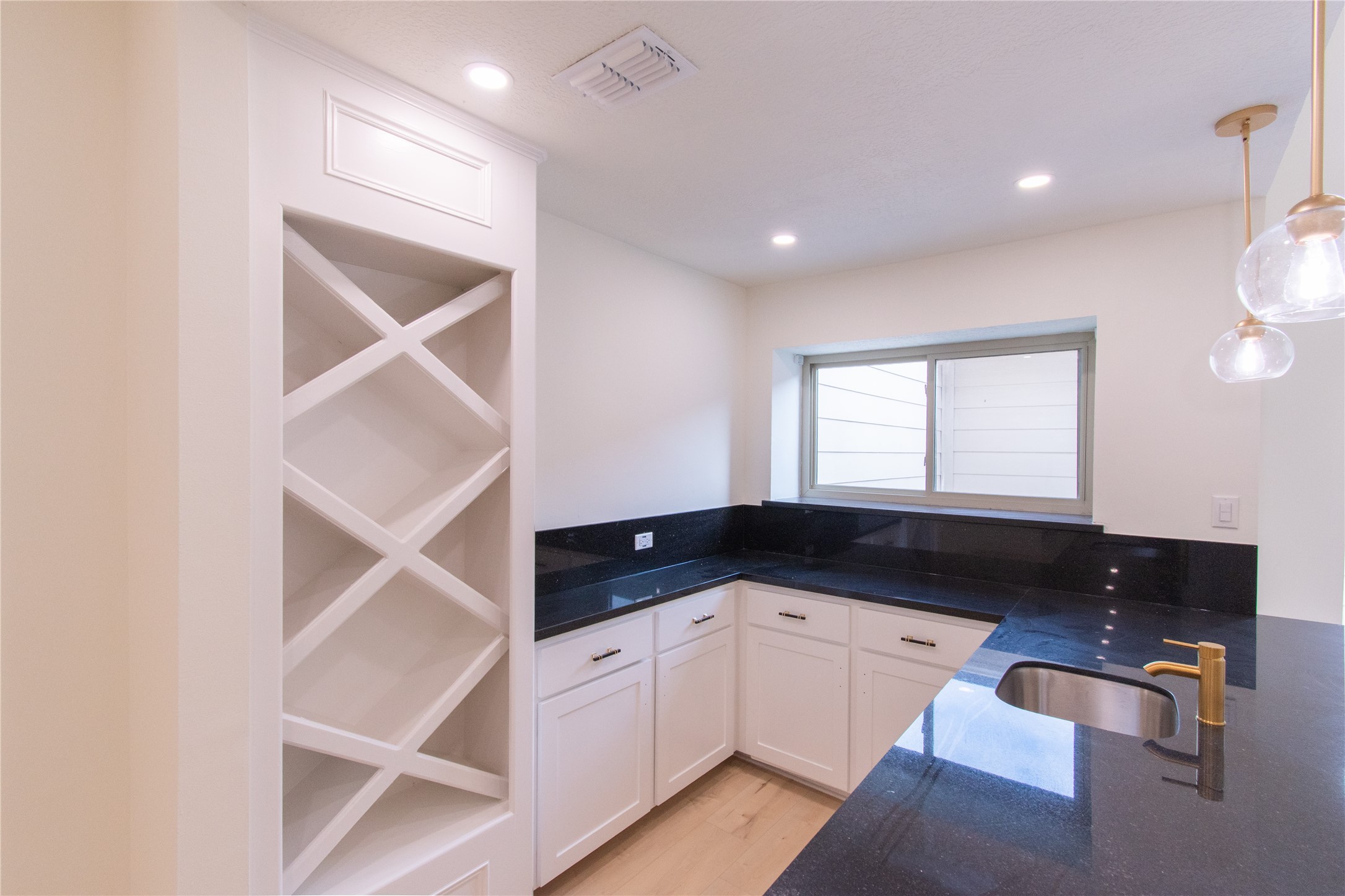 727 Bunker Hill Road, Unit 43 Houston, TX 77024 - Photo 10 of 34 Bar features sleek black countertops, white cabinetry, a built-in wine rack, and stylish pendant lighting. The space is well-lit with recessed lighting and natural light from a large window above the sink.