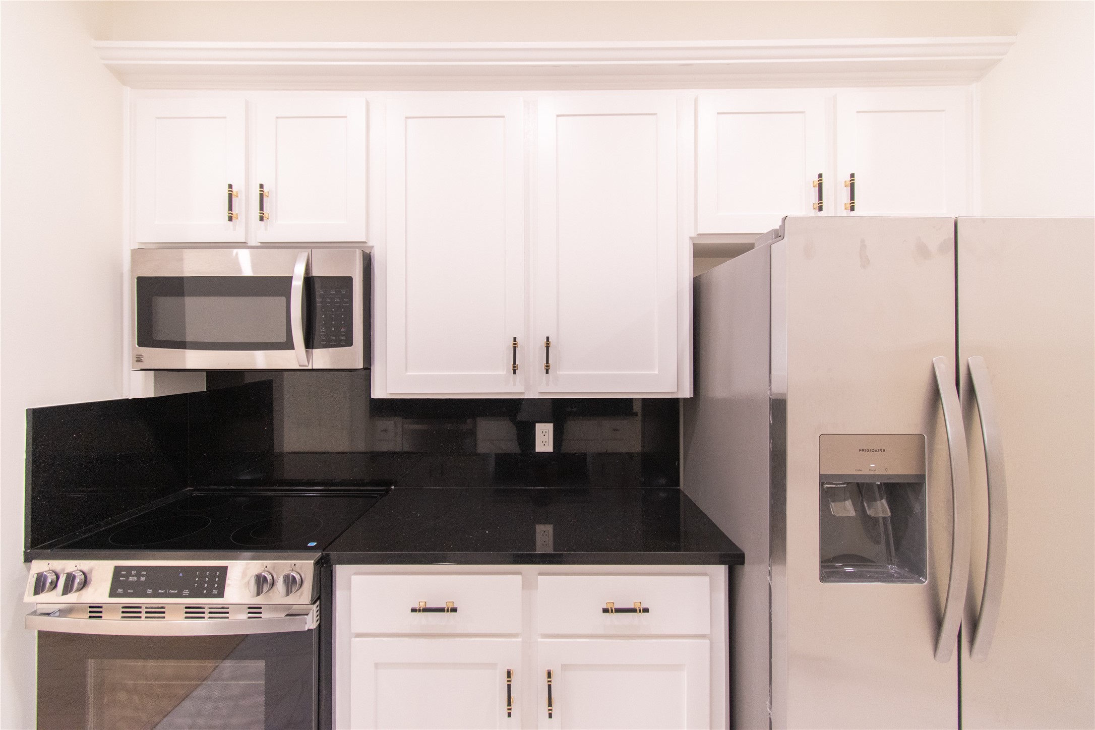 727 Bunker Hill Road, Unit 43 Houston, TX 77024 - Photo 13 of 34 Modern kitchen with sleek black countertops, white cabinetry, and stainless steel appliances, including a fridge, oven, and microwave.