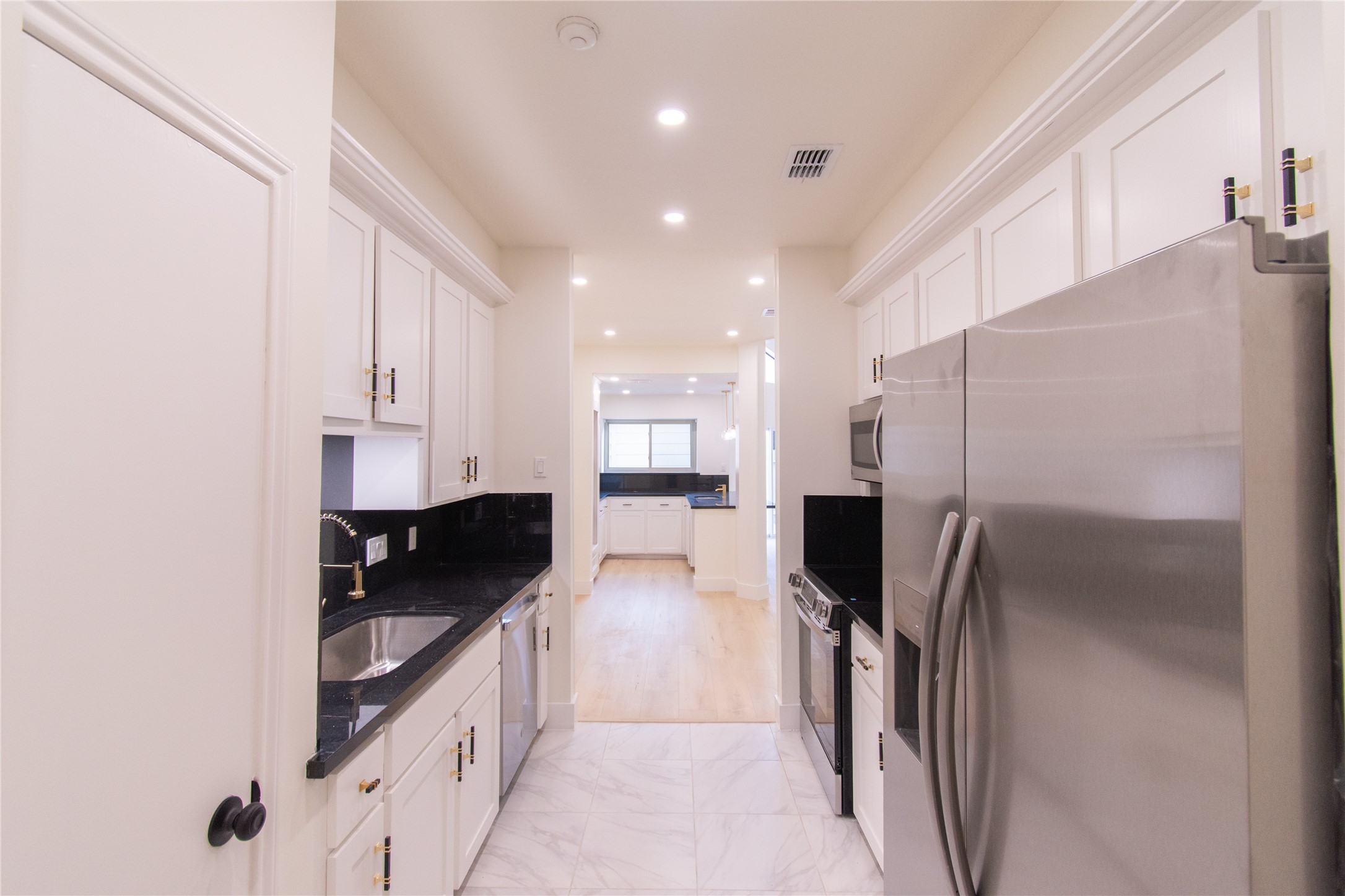 727 Bunker Hill Road, Unit 43 Houston, TX 77024 - Photo 15 of 34 Kitchen features sleek stainless steel appliances, black countertops, and white cabinetry. It has ample lighting and a bright, open layout leading to an adjacent room, creating a spacious and inviting atmosphere.