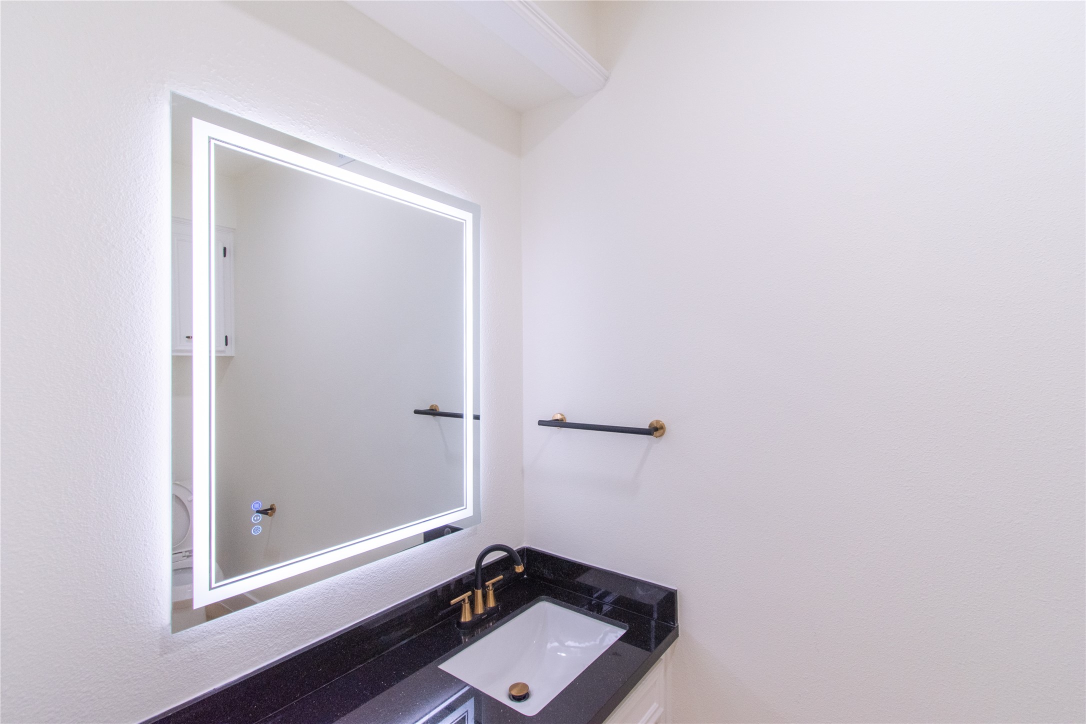 727 Bunker Hill Road, Unit 43 Houston, TX 77024 - Photo 16 of 34 Modern bathroom with a sleek black countertop, under-mounted sink, and illuminated mirror. The design features elegant brass fixtures and a minimalistic style.