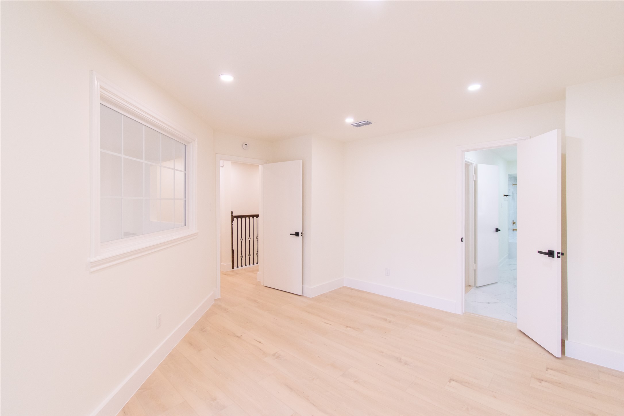 727 Bunker Hill Road, Unit 43 Houston, TX 77024 - Photo 26 of 34 Bright, airy room with light wood flooring, recessed lighting, and white walls. Features a window and two open doors leading to a hallway and a bathroom. Perfect for a bedroom or office space.